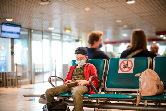 A teenager plays with the phone in a protective medical mask in the airport hall. Protective measures in a pandemic
