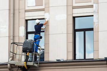 Renovation of the facade of the building. A builder is plastering the wall of a building while standing on a lifting tower. Copy space