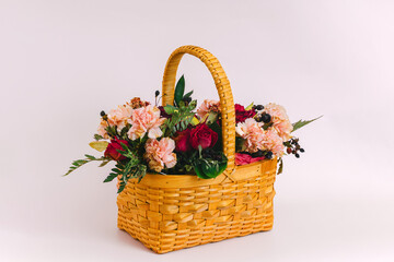 A yellow wicker basket with a bouquet of flowers stands on a delicate pink background. Greeting card.