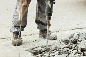 A worker repairs the road surface with a jackhammer on a summer day. Construction works on the...