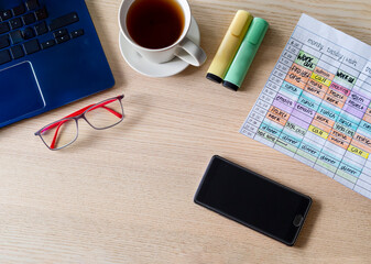 Top view of office workspace desk with laptop, coffee cup, eyeglasses, highlighters, smartphone and weekly calendar with tasks. Time management and time blocking technique for productivity.