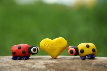 Two ladybugs and a heart made of plasticine close-up. On the hearts is the inscription happy.