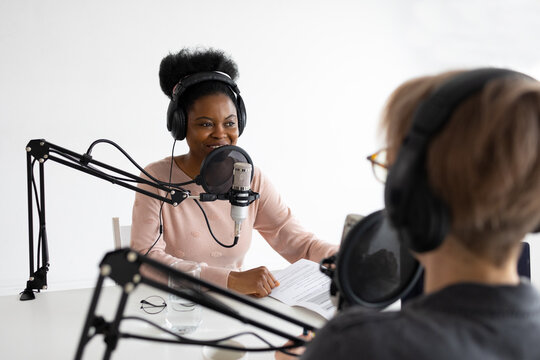 Podcasters, African American and European woman with headphones and microphone recording a podcast in a recording studio, Millennial black woman and white woman creating audio content, confident women