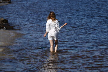 Fototapeta premium Slender woman in white shirt standing in the sea from the back