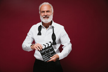 Smiling man in white shirt posing with clapper. Modern adult guy with grey beard in light clothes...