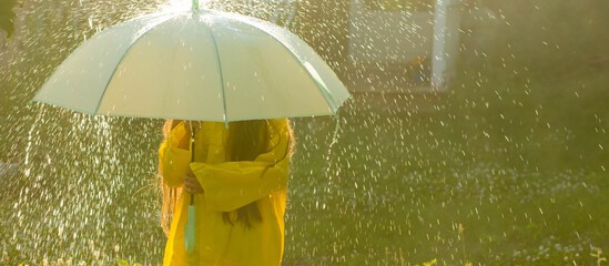 A happy girl with a green umbrella under the summer rain. The girl is dressed in a yellow raincoat...