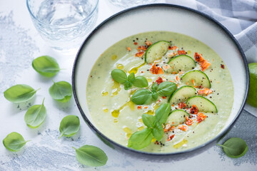 Grey bowl with cold gazpacho made of cucumbers and green basil, studio shot on a white concrete background, selective focus