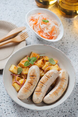 Fried german white sausages served with potato salad, sauerkraut and beer, vertical shot on a beige granite background