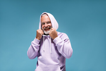 Charming man in light hoodie happily posing on blue background. Handsome guy with beard with tattoos looking into camera and smiling..