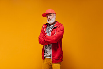 Close up portrait of adult man in red outfit on orange background. Cool handsome guy with grey beard in cap and bright sweatshirt posing..