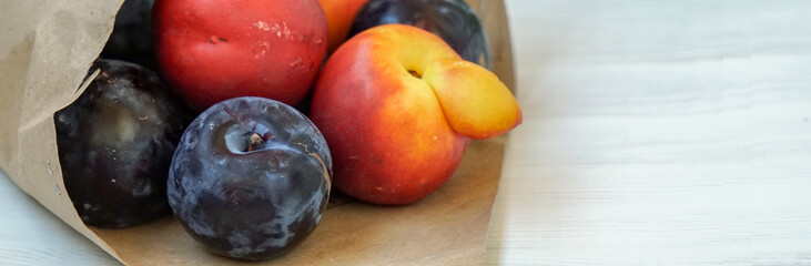 Side view of fresh juicy fruits inside a kraft bag on a light background. Juicy peaches and plums. Copyspace.