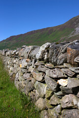 Fototapeta na wymiar Traditional dry stone wall on farmland in the Welsh mountains. On a summers day with blue sky