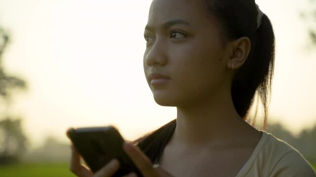 portrait of a beautiful young girl looking while holding a cellphone on sunset