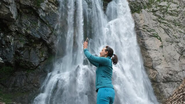 Young Female Tourist Taking Photo Pictures of Beautiful Waterfall by Smartphone. Ecotourism and Travel Lifestyle Concept