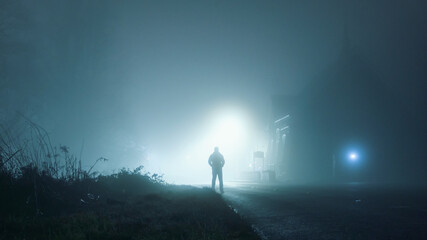 Obraz na płótnie Canvas A man standing next to a church, underneath a street light, on a spooky, country road. On a foggy winters night. Malvern Hills, UK