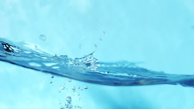 Slow motion video of water waves with splashes and falling drops on a blue background.