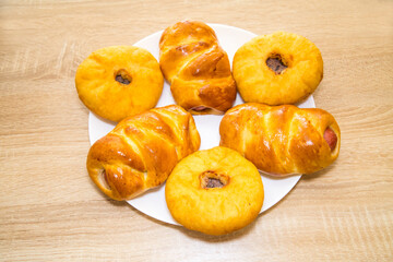 Belyashi with meat and sausages in a delicious yellow dough on a white round plate on a wooden board background. Bakery products national traditional dishes and pastries.