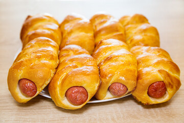 Sausages in a delicious yellow dough on a white round plate on a wooden board background. Bakery products national traditional dishes and pastries.