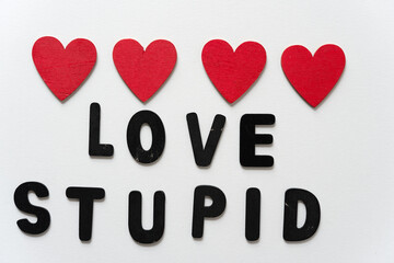 black chalk letters loosely arranged to read love stupid and 4 hand painted red hearts on a white...