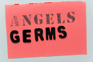 sign with angels written out in stencil font in pencil and the word germs in black chalk letters on coral pink paper