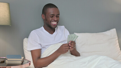 Successful Young African Man Counting Dollar in Bed 