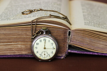 Eine antike Taschenuhr lehnt an einem alten Buch mit vergilbten Seiten
