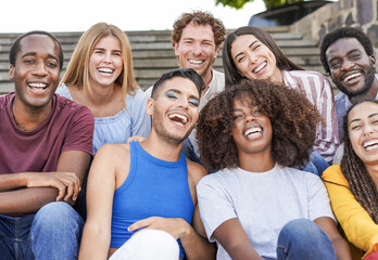 Group of mutliracial  friends smiling on camera while sitting in the city - Millennial people enjoy...