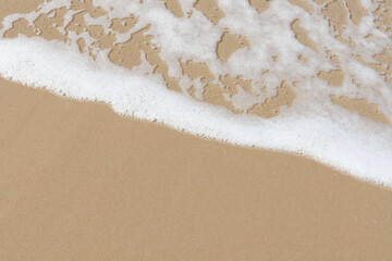 White foam wave on beach top view, beautiful natural scene of tropical summer background for relaxing vacation, ocean waves crashing on sand beach island with copy space.