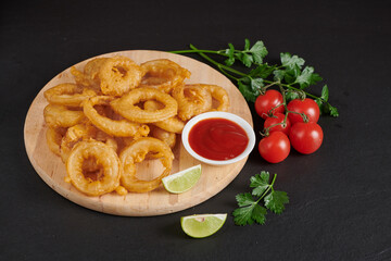 Homemade baked onion rings fries with mayonnaise, Tomato sauce and rosemary on wooden board. fast food products : onion rings on cutting board, on black stone background, unhealthy food.