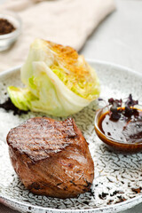 filet mignon on ceramic plate closeup on concrete table. meat with grilled cabbage with bbq sauce