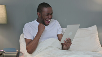 Excited Young African Man Celebrating on Tablet in Bed 