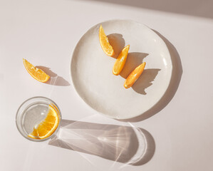 Sliced orange with glass of water and sharp shadows stands on light pink background. Top view flat lay. Caustic reflection effect. Modern trend