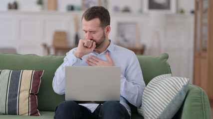 Young Man with Laptop Coughing on Sofa 
