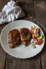 Chicken steak and vegetables in a white plate on a wooden background 