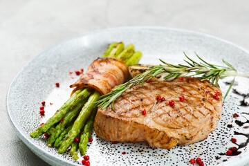 grilled pork steak with asparagus and rosemary leaf on concrete table close up
