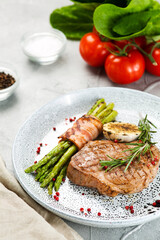 grilled steak with asparagus, rosemary leaf and grilled garlic on plate and ingredients with vegetables on concrete table