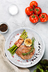 grilled steak with asparagus, rosemary leaf and grilled garlic on plate and ingredients with vegetables on concrete table