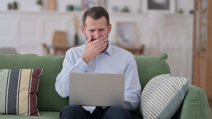 Young Man with Laptop reacting to Failure on Sofa 