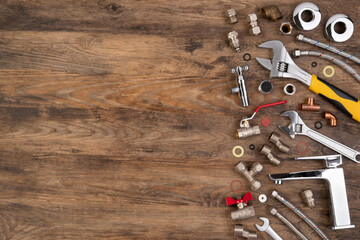 Plumber tools and spare parts on wooden background, top view, flat lay with copy space

