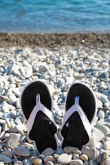 Black flip-flops on the pebble beach with turquoise sea. Summertime. Vacation concept.