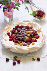 Pavlova cake with cream and berries and a bouquet of flowers on a light background.
