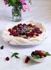 Pavlova cake with cream and berries and a bouquet of flowers on a light background.