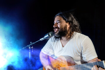 Obraz premium A young Hispanic man singing passionately and playing the guitar at a concert