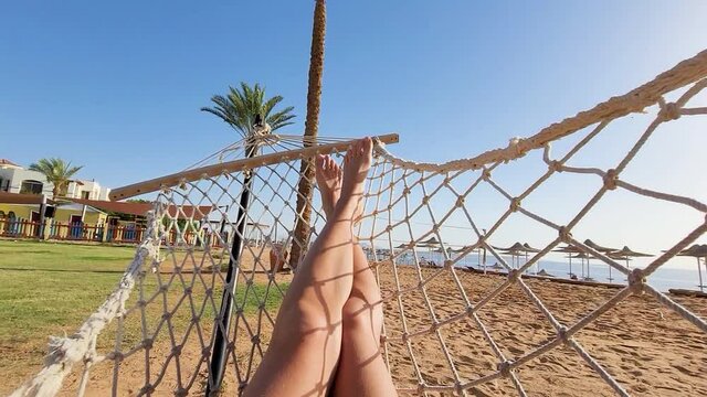 woman relaxing on hammock. Low angle view. Beautiful female feet relaxing in a hammock on the beach against the background of the sky