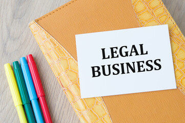 Text legal business on a yellow notebook on a wooden background next to colored markers