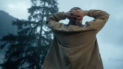 Back view of young handsome man, he is putting hands behind his head and enjoying nature