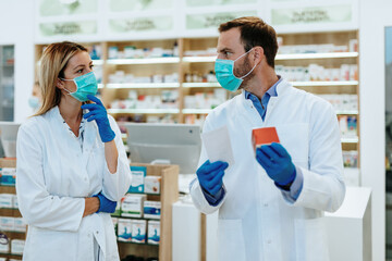Obraz premium Male and female pharmacists with protective mask on their faces working at pharmacy. Medical healthcare concept.