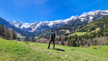 Fototapeta na wymiar A man with a big hiking backpack enjoying the panoramic view on Baeren Valley in Austrian Alps. The highest peaks are sonw-capped. Lush green pasture. Clear and sunny day. High mountain chains.