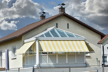 Wintergarten mit dreiseitiger Verglasung und eingebauter Markise an einem Wohnhaus