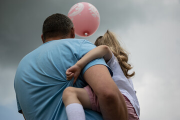 dad holds his daughter in his arms against the background of the sky